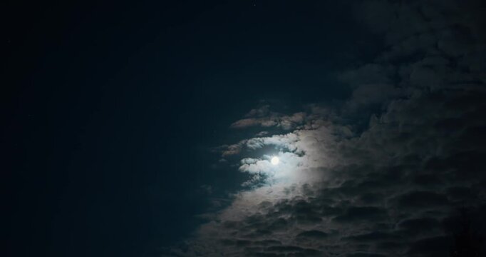Night timelapse of moon behind fast moving clouds, dramatic sky with shifting light and dark layers
