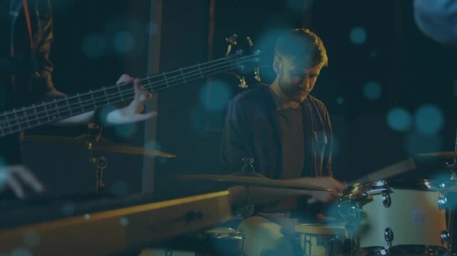 Camera shifting revealing male drummer playing drum kit for music, keys and bass under blue bokeh