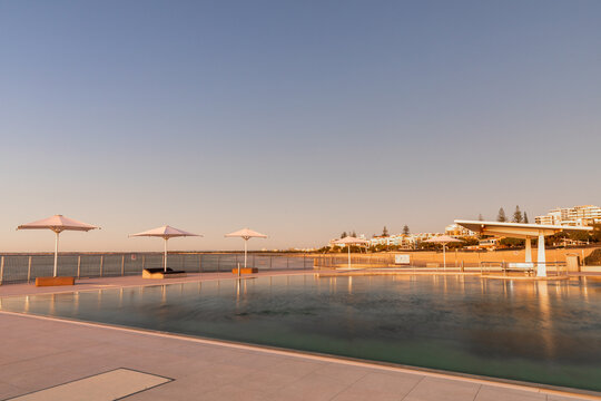 Ocean pool with 4 white umbrellas at sunrise