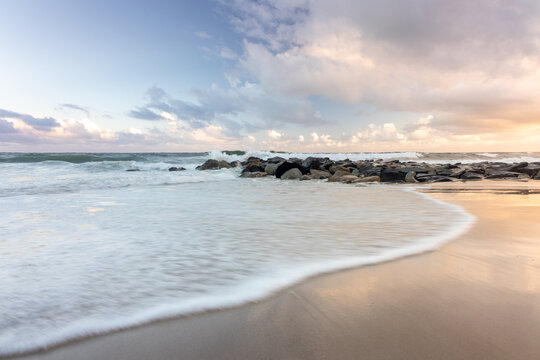 Tide coming in on beach at sunset with rock wall  in background