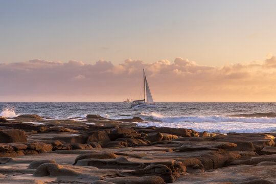 Sailboat on ocean with rocky foreshore and cloudy sky