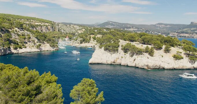 Pleasure boats in Mediterranean calanque with turquoise water and limestone cliffs. Coastal tourism scene in southern France