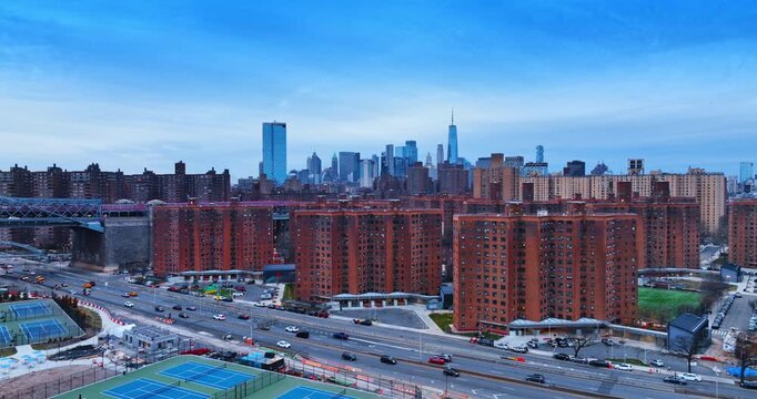 Flying over the tennis courts in the East Side River Park. Approaching the lively highways of FDR Drive and high red-brick residential buildings. Manhattan skyline in the backdrop.