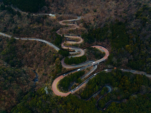 Aerial view of a winding road snaking through forested hills, the asphalt a ribbon of grey against the green and brown landscape, Nikko, Tochigi, Japan.