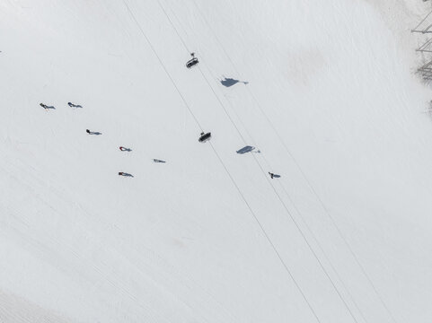 Aerial view of stark white snow punctuated by skiers and their shadows creates a minimalist winter scene, Piano Provenzana, Sicilia, Italy.