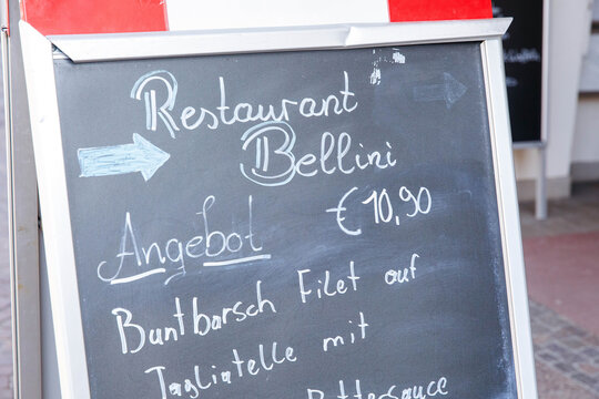 Villach, Austria - March 06, 2026: Restaurant Bellini chalkboard menu displaying daily special for 10.90 with fish dish details and directional arrows outside a dining establishment