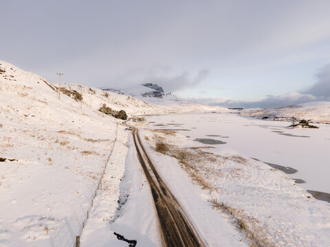 Aerial view of a road cutting through the snow-covered landscape along frozen Loch Fada, near the Old Man of Storr, Isle of Skye, Scotland.