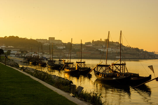 Traditional Rabelo boats loaded with barrels of port wine are moored on the Douro River in Porto, Portugal, at sunset.