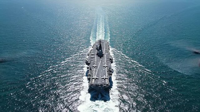 Large aircraft carrier navigates through calm ocean waters, leaving a distinct wake behind, showcasing its powerful presence and advanced naval capabilities in the vast sea