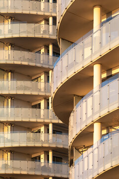 Curved apartments building with stacked balconies and railings catching sunlight creating modern residential architecture pattern and sweeping detail