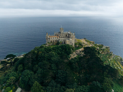 Aerial view of majestic St Michael's Mount stands proud amidst the deep blue sea and lush green foliage, a timeless sentinel of history and nature, Marazion, England, United Kingdom.