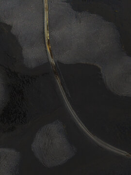 Aerial view of dark and light contrasts create a textured abstract landscape with a thin, curved line cutting through the shadows, Lakagigar, Iceland.