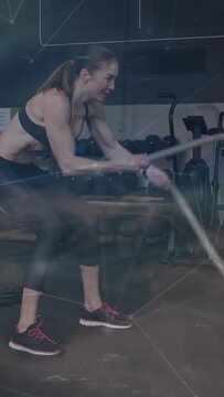 Vertical video: Woman driving alternating waves in gym, gripping rope, causing HUD rep for fitness