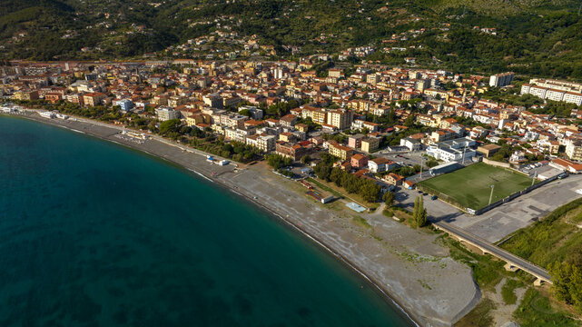 Aerial view on the seafront of Sapri, in province of Salerno, Campania, Italy. Panorama of a beautiful coastal town with colorful buildings, a dark sandy beach, and clear turquoise sea water.