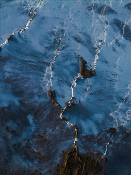 Aerial view of the stark contrast between the dark earth and the bright, snow-covered fissures snaking across the landscape, Grindavikurbaer, Iceland.