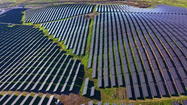 Rows of solar panels stretch across a large field in a rural location. The panels face the sun to generate clean energy during bright daytime hours.