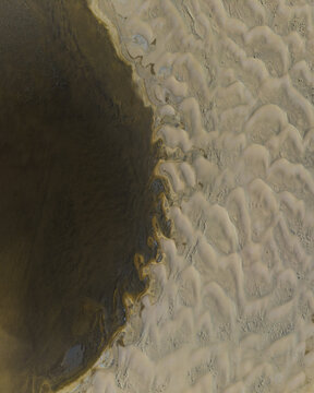 Aerial view of dark, smooth terrain abruptly meets light, rippled dunes, creating a stark contrast of textures and tones on the Westfjords, Iceland