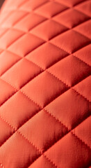 Fototapeta premium Close-up of a red, quilted textile surface with diamond pattern, creating padded effect. It represents craftmanship, luxury and tactile sensation