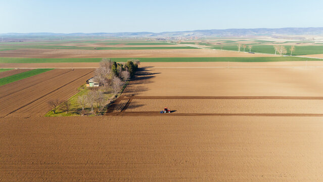 Aerial view of a tractor moving through the vast, tilled fields, carving dark lines into the rich soil under the expansive sky, Sremska Mitrovica, Vojvodina, Serbia.