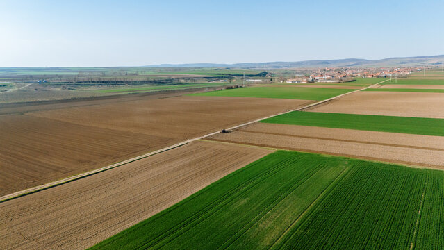 Aerial view of a checkerboard of vibrant green and earthy brown fields, divided by a thin line of road leading to the distant village, Sremska Mitrovica, Vojvodina, Serbia.