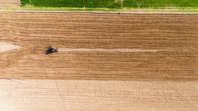 Aerial view of a tractor working the land, creating linear patterns in contrasting soil tones against a vibrant green field, Sremska Mitrovica, Vojvodina, Serbia.