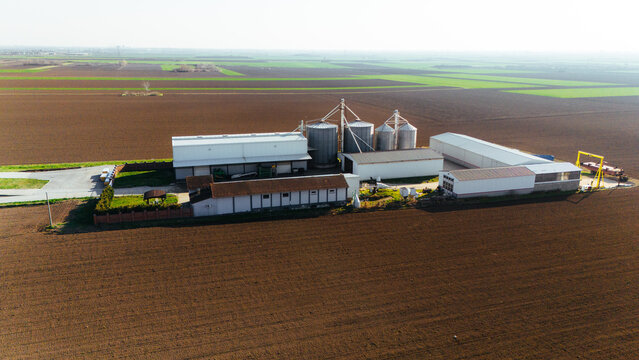 Aerial view of agricultural buildings standing stark against the dark earth, punctuated by fields of vibrant green, Sremska Mitrovica, Vojvodina, Serbia.