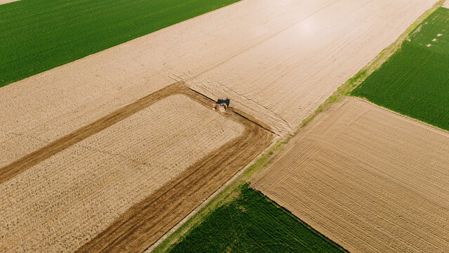 Aerial view of a tractor working the land, carving patterns into the earth with its tracks, surrounded by green fields, Sremska Mitrovica, Vojvodina, Serbia.