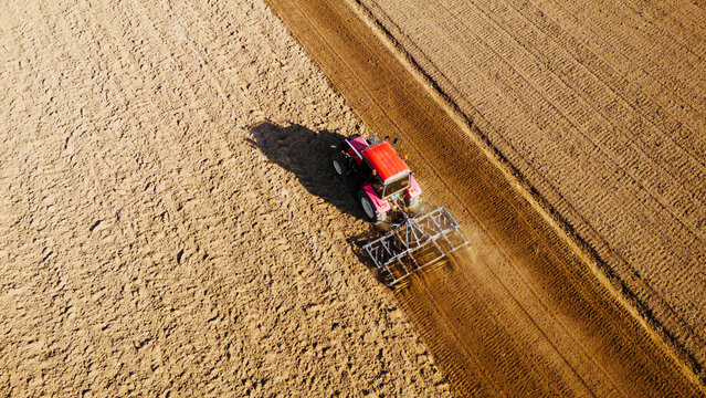 Aerial view of a red tractor against the vast expanse of plowed fields, a scene of agricultural labor, Sremska Mitrovica, Vojvodina, Serbia.