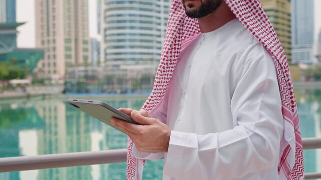 Middle Eastern businessman wearing kandura using a tablet, traditional culture and contemporary business in urban centers, close up.