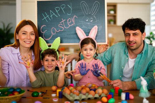 Smiling parents and children showing painted hands and colorful easter eggs while celebrating together at home.