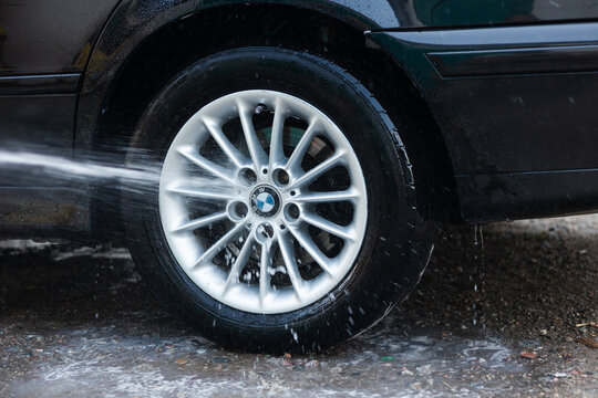 Kant, Kyrgyzstan - July 30 , 2021 : Washing a BMW car alloy wheel with a high pressure water jet at a car wash.