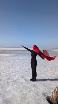 Elegant woman in veil standing on frozen sea at sunset