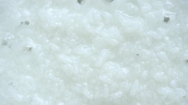 Stirring soft boiled rice soup in a hot pan with a ladle. Top view shot

