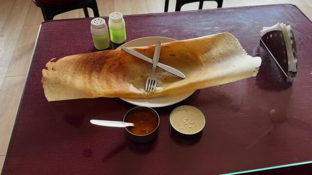 Camera orbiting around a crispy masala dosa served on a plate with coconut chutney and sambar on a restaurant table, showing popular South Indian breakfast food.