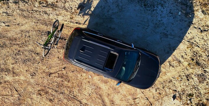 Aerial view of a dark SUV casting a long shadow on the arid landscape, parked next to a fallen bicycle, Fruita, Colorado, United States.