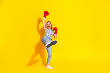 Joyful woman in casual clothing wearing red boxing gloves enthusiastically posing against a bright...