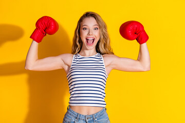 Cheerful woman in red boxing gloves celebrating success against a bright yellow studio background