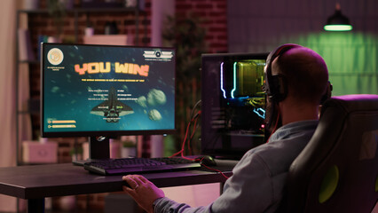 Fototapeta premium Caucasian gamer playing fast paced space shooter simulation enjoying victory after winning difficult gaming competition on pc. Man celebrating feeling victorious in internet multiplayer action game.