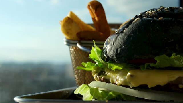 Burger with black bread, black bun against the sea golden fries delightful. Appetizing burger with melted cheese and crispy fries on rustic serving board