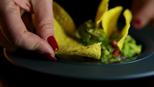 A woman with a red manicure scoops up guacamole Tortilla Chips, Onion Rings, Guacamole and Parmesan Cheese Appetizer, Mexican Cuisine