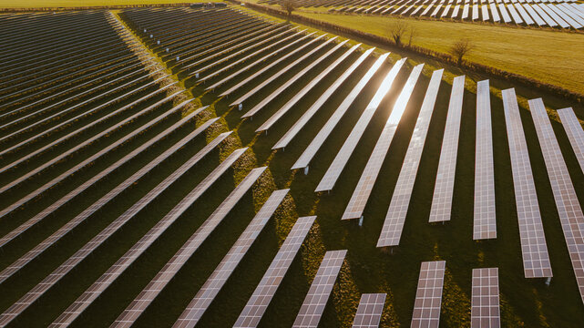 Aerial view of solar panels gleaming under the sun, stretching across the landscape, creating a stark contrast against the green fields, Blandford Forum, Dorset, United Kingdom.