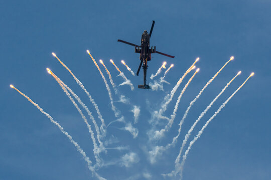 Aerial view of an Apache AH64D helicopter gracefully soaring above, leaving trails of smoke against the vast blue canvas of the sky, Changi, Singapore.