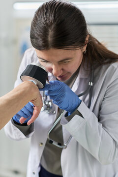 Young woman dermatologist examining skin on patient hand using dermatoscope, wearing medical gloves and lab coat, focusing on detecting possible skin conditions