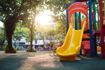medium shot of school playground scene with children playing near colorful slide and climbing frame, bright cheerful atmosphere,