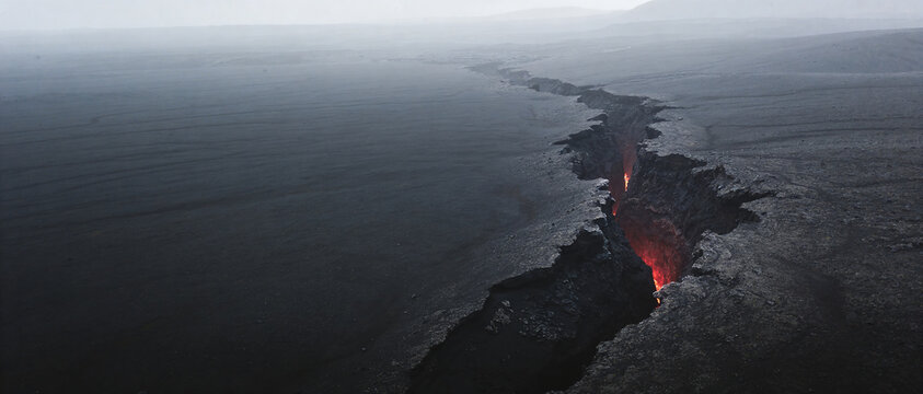 Wide view of deep fissure in dark volcanic valley with glowing magma visible inside crack.