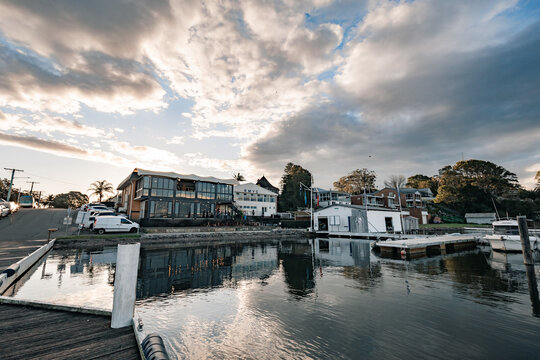 Modern waterfront buildings and marina with boats under a dramatic cloudy sky at sunset