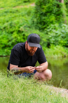 Fisherman getting his rod and line ready to fish crouching on the riverbank