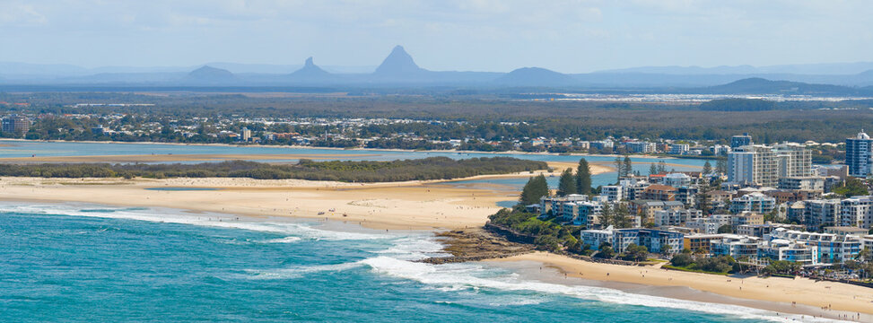 Aerial panorama view of a long sandy beach in front of waterfront buildings and distant mountains
