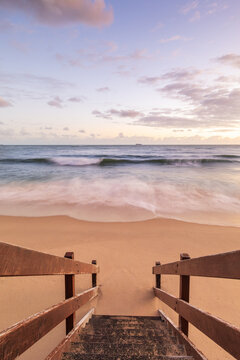 Wooden stairs leading to beach at sunset with waves breaking