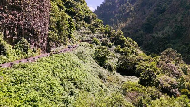 Car moving on a winding cliff road in a deep valley on Madeira, Portugal. Isolated mountain landscape with lush greenery and dramatic rock walls